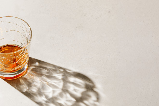 一只水晶威士忌杯在米色背景上，投射出阴影和阳光的反射，简约风格的中性照片，夏季静物的美学俯视图，酒精饮品的折射，光学效应。图片下载