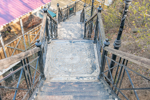 精美设计的锻铁楼梯，背景是红色屋顶建筑。白天的环境中有阴影，照片风格自然。图片下载