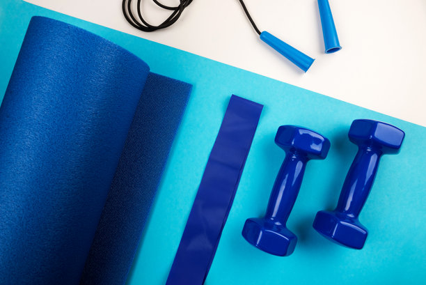 运动配件的概念。蓝色哑铃、蓝色瑜伽垫和其他运动器材的俯视照片，背景为蓝色和白色。图片下载