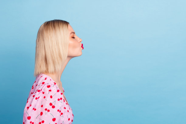 可爱迷人的女孩侧面照片，穿着时尚的粉色印花衣服，背景为蓝色，留有空白空间。图片下载