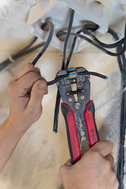 电工使用剥线钳小心地去除电线的绝缘层，为家庭装修项目中的连接做准备。竖版照片图片下载