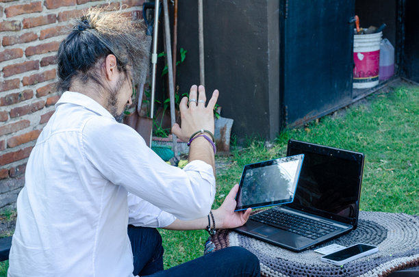 男子在户外挥手并通过笔记本电脑进行视频通话，照片从背面拍摄。图片下载