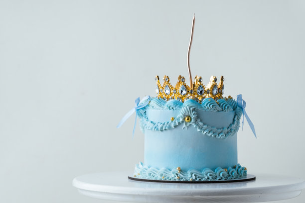精致的兰贝斯复古风格蛋糕，配有蓝色奶油奶酪糖霜，装饰有奶油花纹。柔软的生日蛋糕，上面装饰着金色皇冠和蜡烛，背景为白色。图片下载
