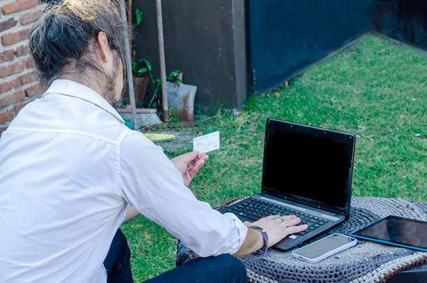 男子在户外使用信用卡，手持手机和数字平板，照片从背后拍摄。图片下载