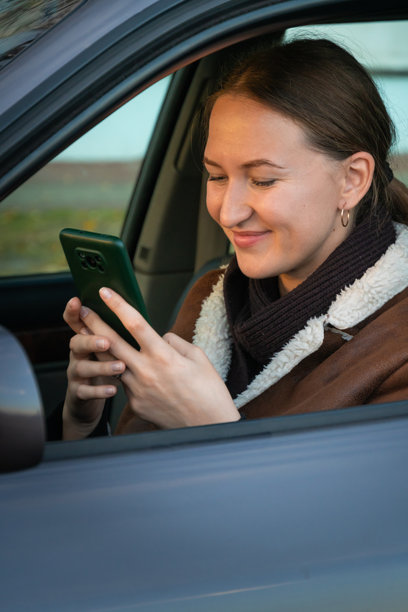 年轻女子坐在车内，查看智能手机，庆祝成功，双手举起，面露喜悦。竖版照片图片下载