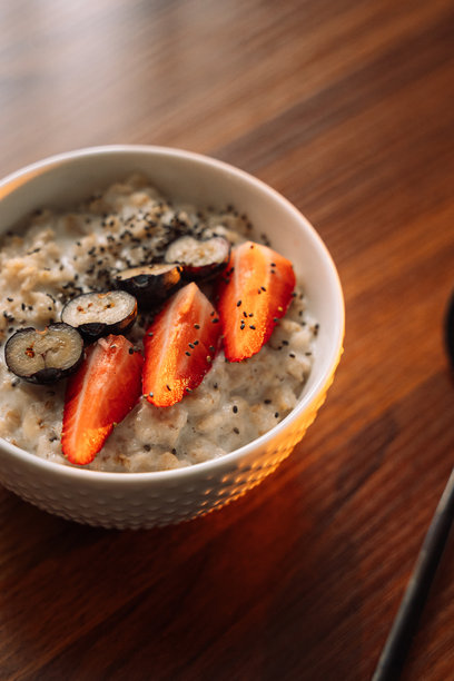 白色碗中的草莓燕麦粥，背景为木质纹理，竖版照片图片下载