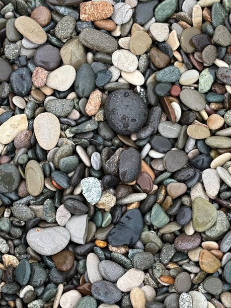 特写照片展示了在海滩上收集的各种形状和大小的多彩湿卵石和石头，展现了自然的纹理和变化。图片下载