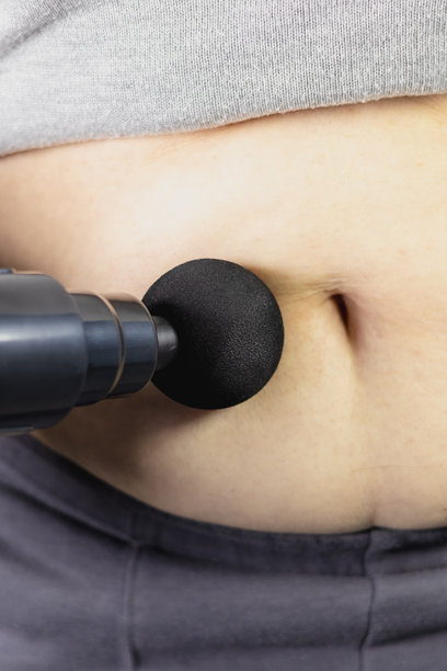 女性使用冲击按摩枪在自己肥胖的腹部进行抗 cellulite 按摩的竖版照片。腹部超重问题。物理治疗，自我按摩工具。健康护理。特写。图片下载