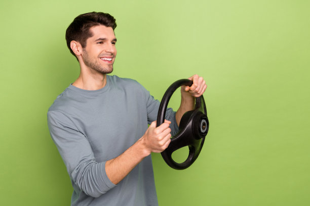 搞笑的年轻棕发男孩穿着灰色毛衣，开车的个人资料照片，背景为绿色。图片下载