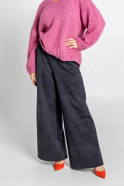 模特外貌的美丽女性肖像。女孩穿着粉色毛衣、黑色裤子和红色鞋子，背景为灰色。时尚妆容的漂亮女性在摄影棚中摆姿势。竖版照片图片下载