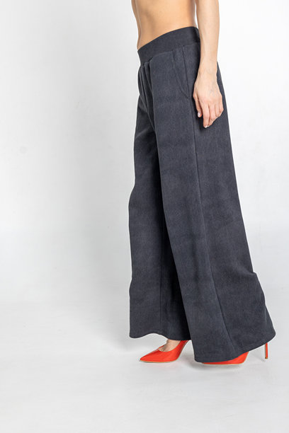 模特外貌的美丽女性肖像。女孩穿着黑色裤子，脚踩红色鞋子，背景为灰色。竖版照片。图片下载