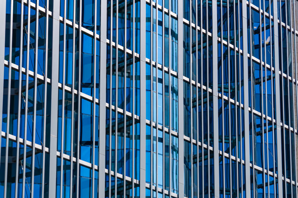 现代办公大楼外立面，配有玻璃立面和金属构件。窗户中的光线和天空反射形成了动态的几何图案。非常适合与建筑、商业和房地产相关的项目的照片。图片下载