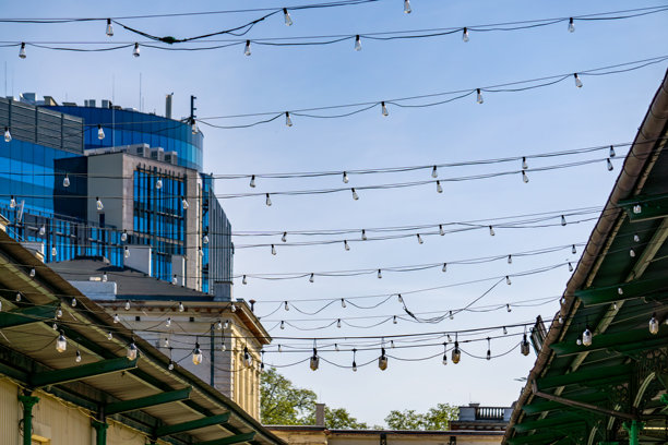 现代玻璃建筑在背景中，传统屋顶在两侧，城市空间上方悬挂着灯光。照片展示了现代与历史建筑之间的对比，以及城市公共空间的温馨氛围。图片下载