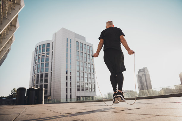 穿着T恤、短裤和运动鞋的退休爷爷在城市户外跳绳的背影照片图片下载