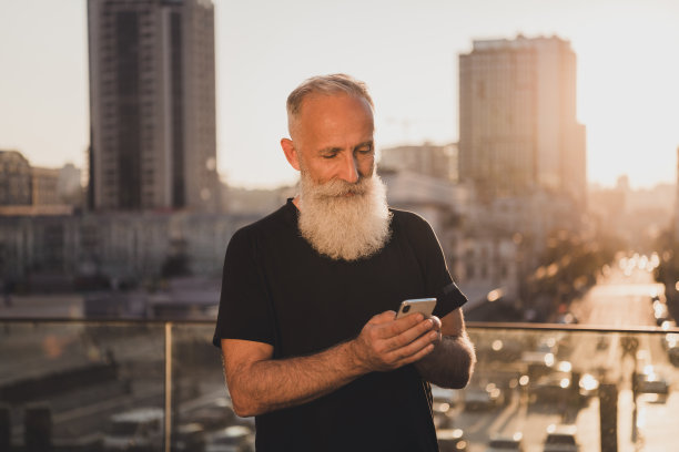 穿着运动风格T恤的胡须老年人影响者在城市户外准备电话博客的照片图片下载