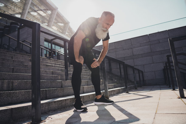 全身照片，疲惫的老年灰发男士穿着黑色T恤、短裤和鞋子，在体育场外。图片下载