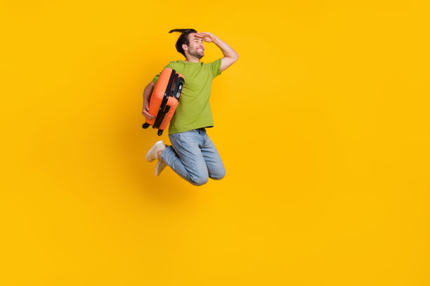 年轻男子穿着毛衣的全身侧面照片，空旷的行李箱，旅游，背景为黄色。图片下载