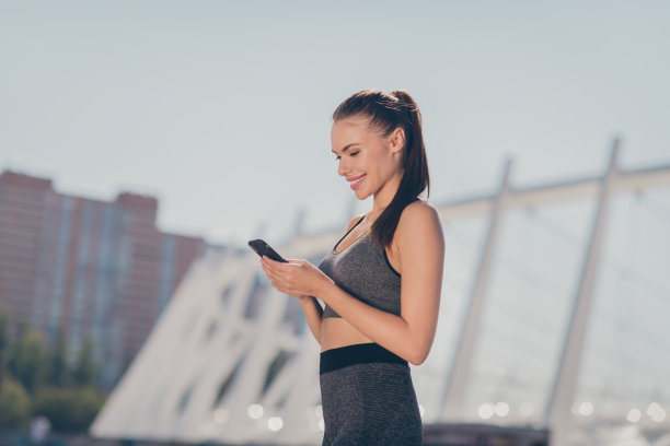 运动女性在市中心使用智能设备的侧面照片，正在通过运动应用程序计步。图片下载