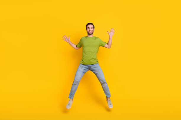 年轻男孩在黄色背景下充满活力地跳起并挥手问好，照片为全身照。图片下载