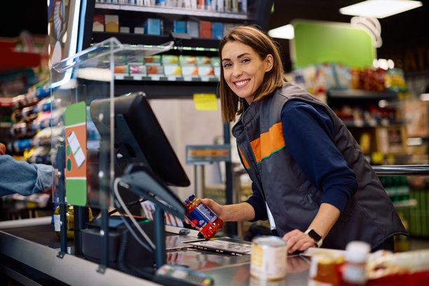 快乐的收银员在超市结账时扫描商品并看向镜头。图片下载