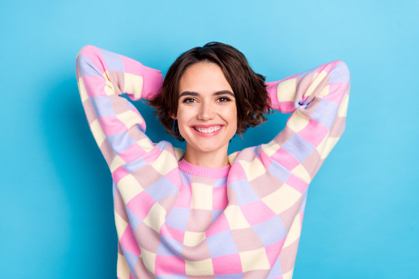 高角度俯视照片，年轻快乐的女士双手放在头后，放松地坐在蓝色背景下。图片下载