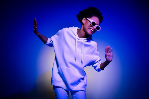 穿着卫衣、戴着深色眼镜的甜美漂亮女性在蓝色背景下微笑跳舞的照片图片下载