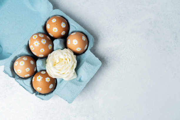 手绘的复活节彩蛋，带有雏菊图案，放在蓝色纸箱中，旁边有白色玫瑰。轻背景上的复活节构图。图片下载