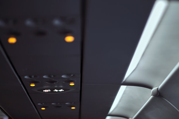 飞机客舱乘客座位上方的禁烟标志灯亮起，表示飞行中禁止吸烟，照片有噪点且部分模糊。图片下载