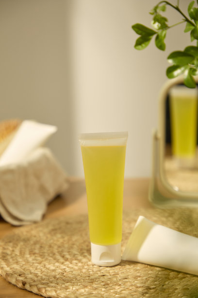 一张垂直照片，展示了一个装有新鲜柠檬提取精华的管子。另一个白色的乳霜管放置在藤编地毯上。后面是一个桌面镜子，反射出物体的影像。图片下载