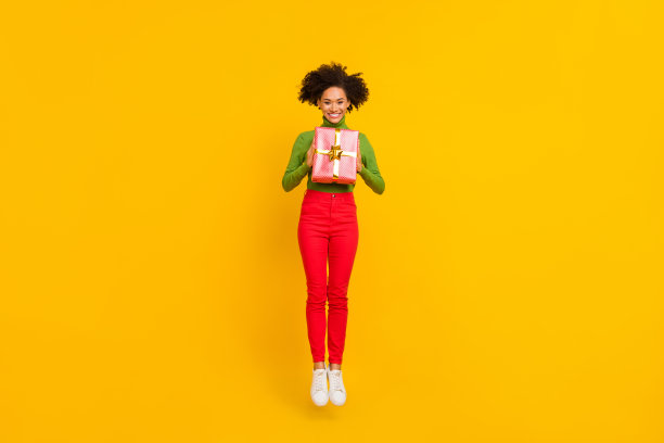 年轻快乐的女孩穿着毛衣，充满活力地在黄色背景下接收礼物盒的全身照片图片下载