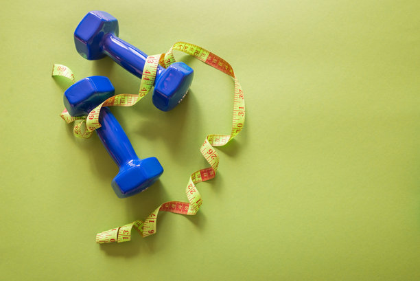 健身概念。照片中有一卷卷尺和哑铃，背景为纯绿色。图片下载