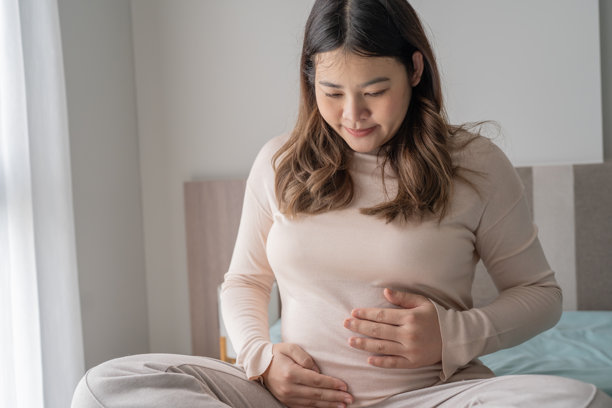 怀孕的亚洲女性双手放在肚子上，关心着她的宝宝和自己的健康。美丽快乐的孕妇，温柔的怀孕心情照片。图片下载