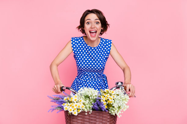 年轻女士骑自行车，穿着衬衫，背景为粉色，欢呼的照片图片下载