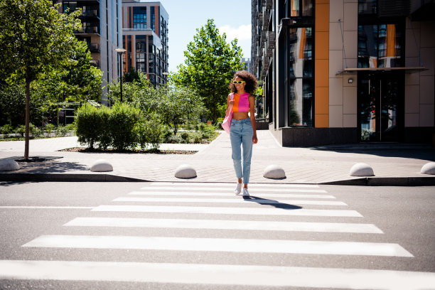 穿着色彩鲜艳衣服的年轻漂亮女性在城市公园的街道十字路口散步的全身照片图片下载