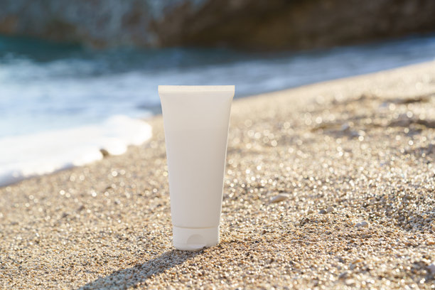 白色的护肤霜样品管放在湿沙滩上，背景是海洋。皮肤和身体护理概念，防晒，美容产品。适合您设计的图片。图片下载