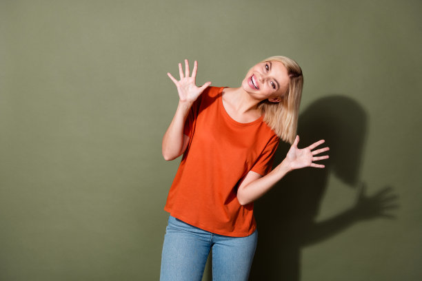 漂亮年轻女孩的照片肖像，双手举起掌心，兴奋地穿着时尚的橙色服装，背景为卡其色。图片下载