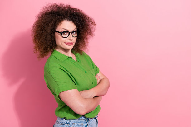 自信的年轻女孩照片肖像，双手交叉，穿着时尚的绿色服装，背景为粉色。图片下载