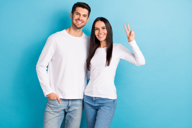 可爱的年轻男女在蓝色背景下拥抱，摆出V字手势，穿着时尚的白色服装拍摄的肖像照片。图片下载