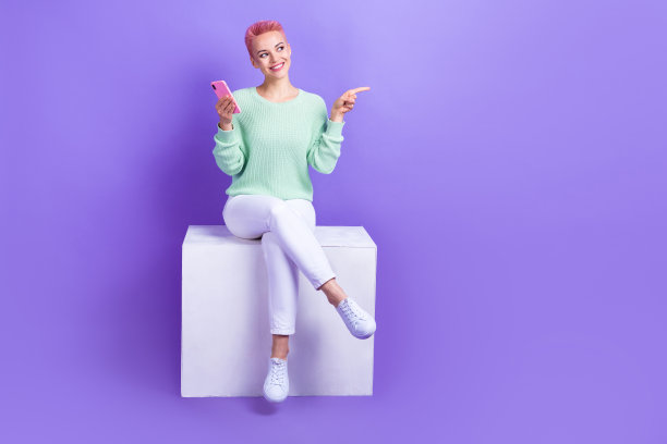 梦幻闪亮的女孩穿着青绿色毛衣，使用现代设备发短信，背景为紫色，显示空白空间的全身照片图片下载