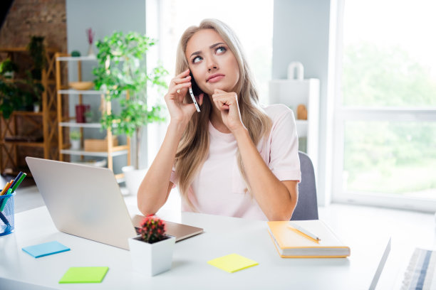 一位年轻魅力女性的照片肖像，她在现代办公室内不满地通过电话工作，穿着白色T恤，办公室环境时尚。图片下载