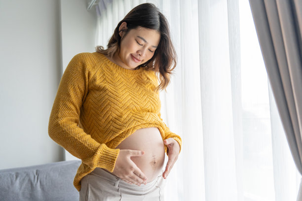 怀孕的亚洲女性双手放在肚子上，轻抚着她的宝宝，关心自己的健康。美丽快乐的孕妇，温柔的怀孕心情照片。图片下载