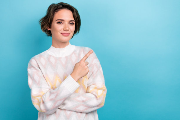 穿着时尚白色衣服的迷人年轻女性在蓝色背景前指向空白处的照片肖像图片下载