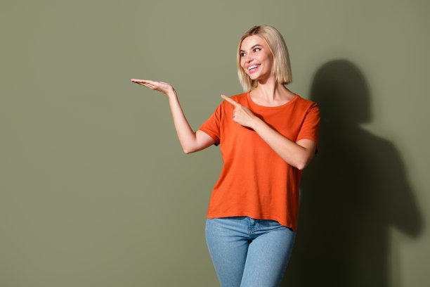 漂亮年轻女孩的照片肖像，手指指向空白处，穿着时尚的橙色服装，背景为卡其色。图片下载