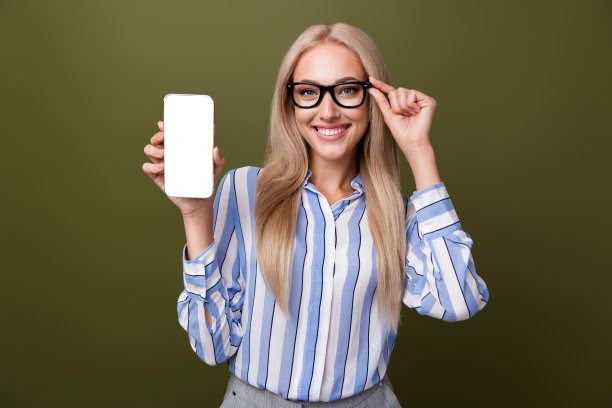 金发可爱年轻女士的照片肖像，手持电话屏幕，触摸眼镜，穿着时尚条纹服装，背景为卡其色。图片下载