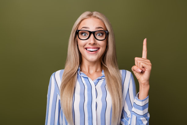 金发可爱年轻女士的照片肖像，兴奋地指向上方，穿着时尚的条纹服装，背景为卡其色。图片下载