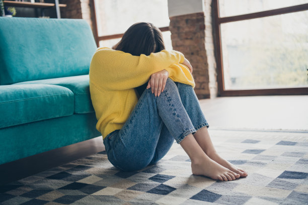 坐在现代公寓地毯上的不满人士全身侧面照片，情绪低落，正在哭泣。图片下载