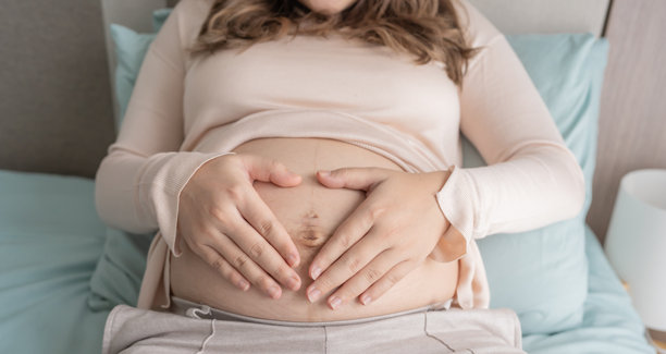 怀孕的女人双手放在肚子上，关心着她的宝宝和自己的健康。美丽快乐的孕妇，温柔的怀孕心情照片。图片下载