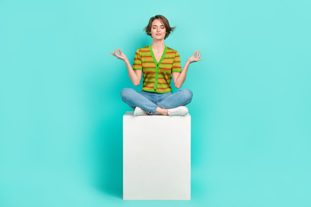 全身照片，平静安详的人坐在讲台立方体上冥想，背景为青绿色。图片下载