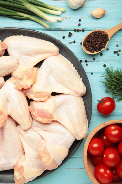 黑色盘子上的生鸡翅与烹饪所需的食材，背景为蓝色木纹。竖版照片图片下载