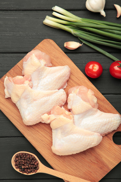 生鸡翅与烹饪所需的食材放在黑色木质背景上的木砧板上。竖版照片图片下载